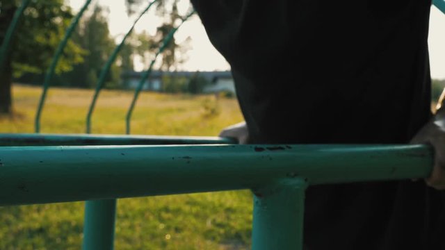 Young man doing push-ups from parallel bars on the playground in a natural public park. Sunset time.