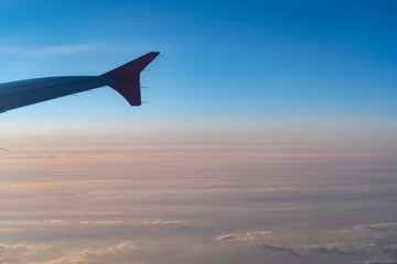 Up in the air, view of aircraft wing silhouette with dark blue sky horizon and cloud background in sun rise time, viewed from airplane window