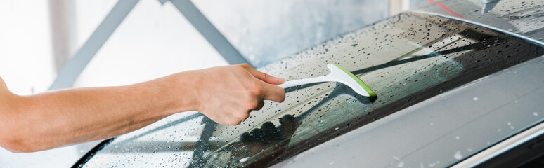 panoramic shot of man holding squeegee and washing wet car window