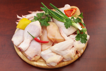 Assortment of diffeent chicken meat parts with vegetables on round cutting board