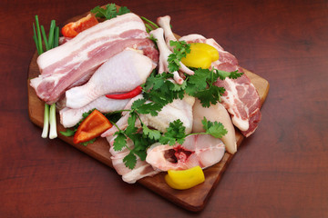 Assortment of meat, chicken and fish with vegetables and greens on wooden board on brown table