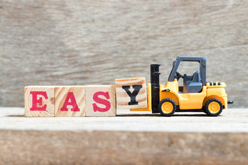 Toy forklift hold letter block y in word easy on wood background