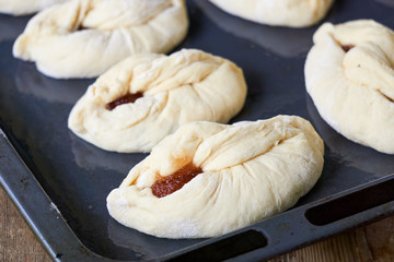 Raw buns with jam on a baking sheet