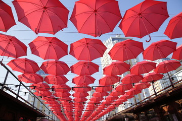 Fototapeta premium Red umbrellas against the blue sky and the bright building. Abstract background with umbrellas