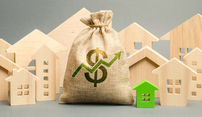 Money bag with arrow up and miniature wooden houses. The concept of rising property prices. High...