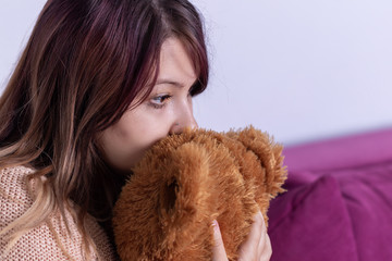 Unhappy lonely depressed woman at home, she sitting on couch and covering her face on stuffed animal, depression concept 