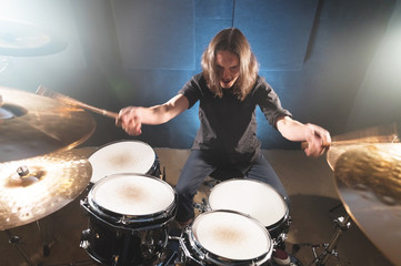 Portrait of a long-haired drummer with chopsticks in his hands sitting behind a drum set. Low key. Concepts of the creative freedom of the millenial generation