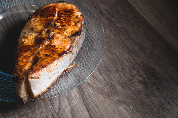 Close-up one grilled cum salmon keta fish steak on a glass transparent plate on a dark wood table background. A little overdone dish. Sea food for lovers of fried