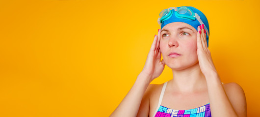 Photo of young woman swimmer in cap for swimming glasses on empty orange background