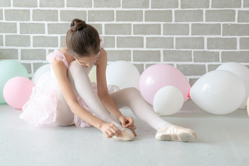 Cute beautiful young little girl ballerina dancer in pink leotard and tutu ballet dress costume sitting on the floor in studio wearing and tie her ballet slipper shoe for ballet dance practice. © CandyRetriever 