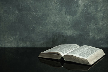 Bible on a black glass table. Beautiful gray wall background. - Powered by Adobe