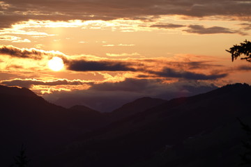 beautiful sunset with orange sky, clouds and tree silhouette in the mountains