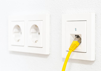 Yellow network cable in wall outlet for office or private home lan ethernet connection with power...