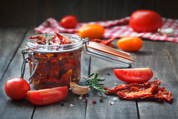 Sun-dried tomatoes with herbs and garlic in glass jar. Healthy food ingedients for delicous cooking. Rustic wooden background.