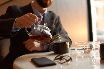 Close up of a ma in suit pouring tea into a cup.