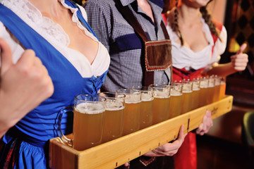 two attractive young girls and a man in traditional Bavarian clothes hold in their hands a lot of glasses of beer on the pub background during the celebration of the Oktoberfest