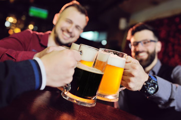 a group of young men's friends in a bar or pub drinking beer with glasses and watching football during the celebration of Oktoberfest