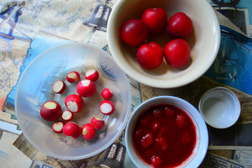 Kitchen. Round plates with red products are on the table. Plums, radishes and strawberry jam. The view from the top.