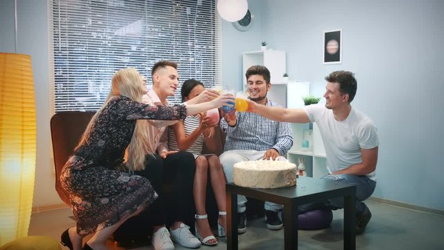 Multi-ethnic young people making toasts with dry uce cocktails on birthday party. There is a big birthday cake with candles on table. Elements of this image furnished by NASA.