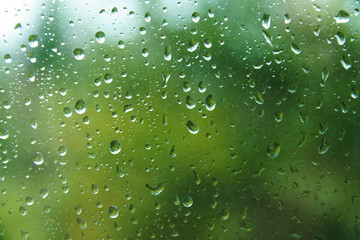 Fototapeta na wymiar Beautiful view from window at dim outlines nature backdrop. Water drops on glass with blurred edges. View from window on rainy day. Rain drop on windowpane with blur tree background.