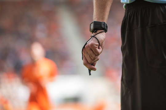 Hand of soccer referee with wristwatch and whistle.
