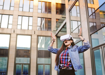 Beautiful girl in denim jacket with long hair playing VR game standing in front of glass building