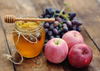 honey in a beautiful jar, wooden spoon spindle, grapes and apples on a wooden background