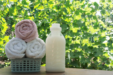 Basket full of clean washed towels and bottle of softner on the wooden rustic table against green garden.Natural light