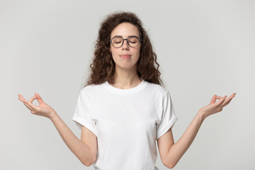 Tranquil young woman meditating pose on grey studio background