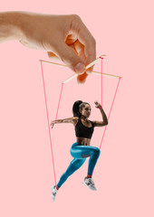 Woman like a puppet in somebodies hands on coral background. Concept of unfair manipulation,...