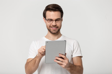 Millennial guy in glasses using tablet isolated on grey background