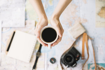 Top view of a person's hand holding coffee cup over the blurred world travel map