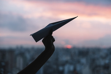 Silhouette of a person's hand holding paper airplane against dramatic sky