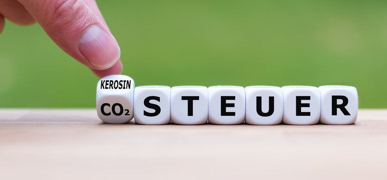 Hand dreht einen W&uuml;rfel und &auml;ndert das Wort CO2-Steuer in Kerosin-Steuer (oder umgekehrt).
