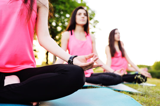A group of young slender, beautiful girls doing yoga or fitness on fresh grass against the backdrop of nature and sunset