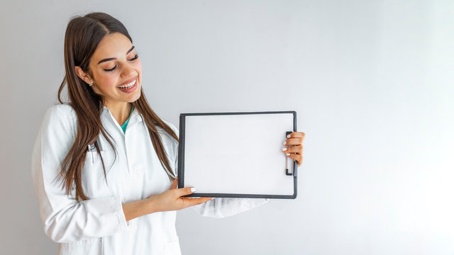 Cheerful young female doctor showing clipboard with copyspace for text or design, isolated over grey background. Young happy smiling doctor showing folder with diagnosis