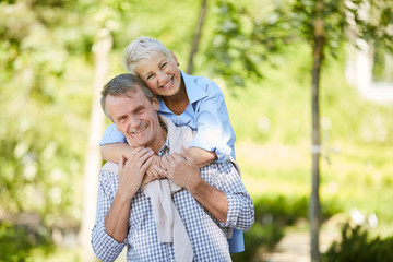 Portrait of carefree senior couple smiling at camera while enjoying date outdoors in Summer park,...