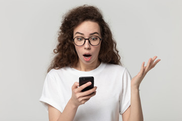 Fototapeta premium Amazed woman looking on smartphone screen posing on grey background