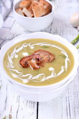 Vegetable cream soup with asparagus and peas garnished with cream and roasted champignons and a bowl of croutons next to it