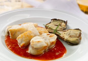Merluza  con alcachofas  y salsa de tomate, sobre fondo blanco. Hake with artichokes and tomato sauce, on a white background.