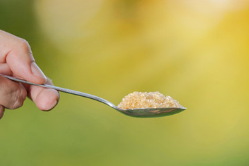 Hand is holding a spoon with sugar on a natural background