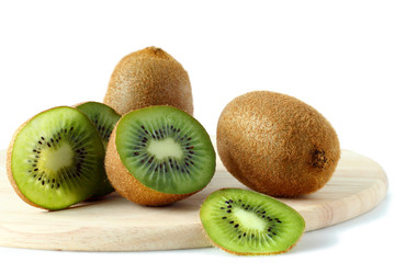 Kiwi fruit whole and sliced on a wooden round board on a white background.
