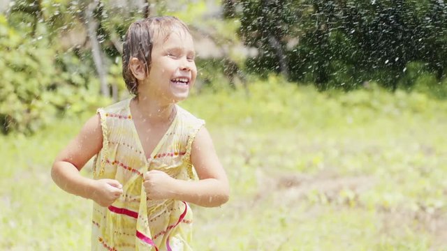 Laughing little girl dancing under the spray from a garden hose
