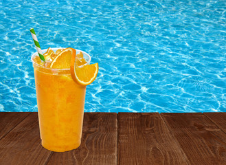 Fresh orange juice with straw and slice in plastic take away cup on pool background
