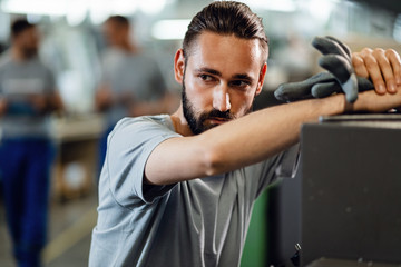 Fototapeta premium Young factory worker leaning on CNC machine and thinking of something.