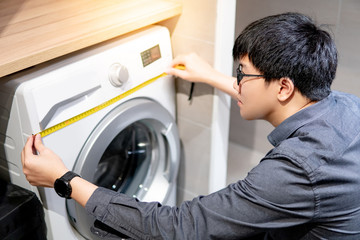 Asian technician man using tape measure for measuring washing machine under wooden counter....