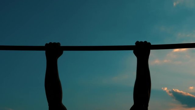 A young man makes pull-ups on the horizontal bar. Silhouette of a man against the background of dark blue cloudy sky.