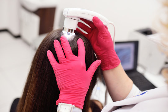 doctor dermatologist diagnoses the structure of the hair of a young pretty girl with a special tool - a trichoscope. Trichology, trichogram
