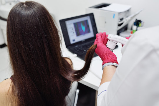 doctor dermatologist diagnoses the structure of the hair of a young pretty girl with a special tool - a trichoscope. Trichology, trichogram