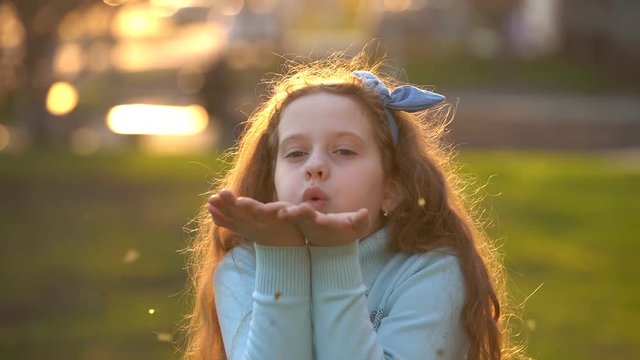 Little girl blowing gold confetti with her hand. Holiday, happy childhood, healthy lifestyle concept.